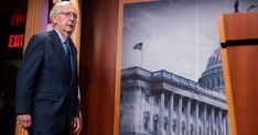 a man in a suit and tie standing next to a poster with the u s capitol building on it