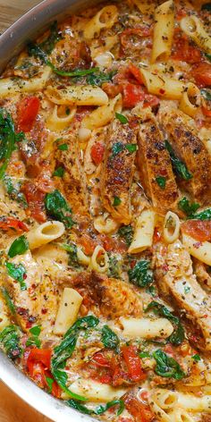 pasta with chicken, spinach and tomatoes in a skillet on a wooden table