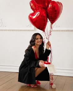 a woman kneeling on the floor holding two heart shaped balloons