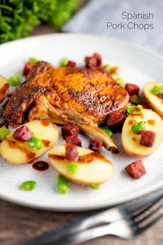 a white plate topped with meat and potatoes on top of a wooden table next to a fork