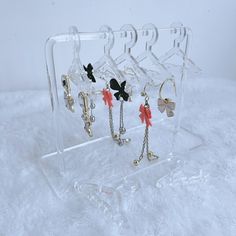 four pairs of earrings are hanging on a clear display case with chains and charms attached to them