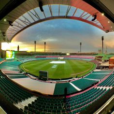 an empty baseball stadium with the sun setting on the field and clouds in the sky