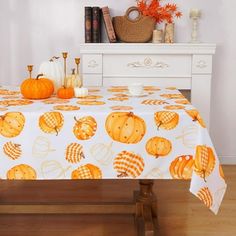 an orange table cloth with pumpkins on it in front of a white dresser and bookshelf