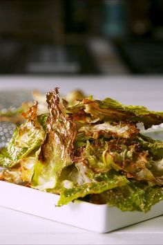 a white bowl filled with lettuce on top of a table next to a silver grater