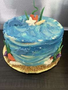 there is a blue cake with seaweed and starfishs on the top it sits on a gold plate