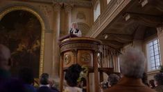 a man standing at the top of a pulpit in a church with other people watching