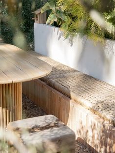 a wooden bench sitting next to a table and some plants on top of a stone wall