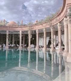 an indoor swimming pool surrounded by columns and arches with white drapes on the ceiling