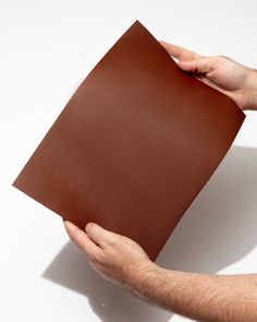 a person holding up a brown piece of leather