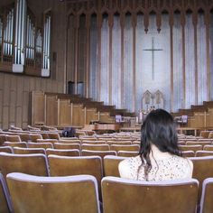 a woman sitting in an empty church looking at the pews and pipe organ behind her