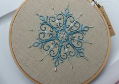 an embroidered snowflake is displayed on a piece of fabric in a wooden hoop