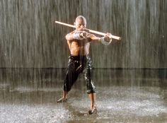 a shirtless man holding a baseball bat in front of a shower of water and rain