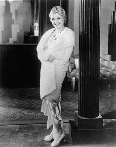 an old black and white photo of a woman standing next to a pillar