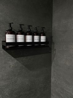 four bottles of hand soap on a shelf in a dark room with concrete walls and flooring