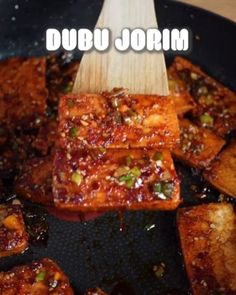 some food is cooking in a skillet with a wooden spoon on it and the words, dubu jorn above it