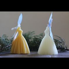 two soaps in the shape of dresses are sitting on a table next to pine branches