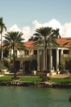 a large house with palm trees in front of it on the side of a body of water