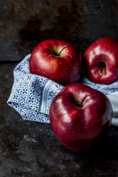 three red apples sitting on top of a blue cloth