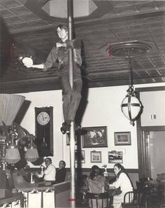 an old black and white photo of a man standing on a pole in a restaurant