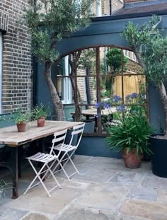 an outdoor dining area with potted plants and chairs in front of the table, surrounded by trees