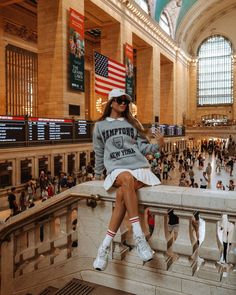 a woman sitting on top of a ledge in a train station with lots of people