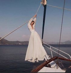 a woman in a white dress is standing on the front of a sailboat with her arms up