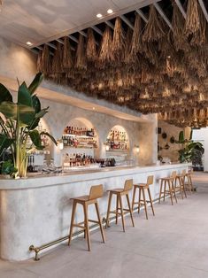 an indoor bar with chairs and plants on the counter, along with hanging straws