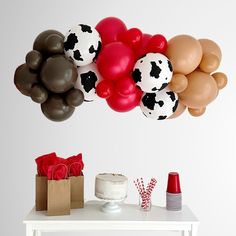 a table topped with lots of balloons next to a cake and gift bags on top of it