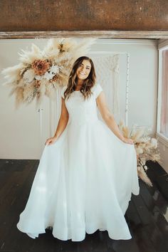 a woman in a white dress standing with her hands on her hips and holding flowers