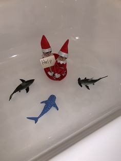 two elfs are sitting in the bathtub with dolphins and shark toys around them