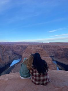 a woman sitting on the edge of a cliff looking out over a canyon and river