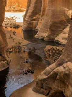 some people are standing in the water near large rocks and sand cliffs, while others walk around them