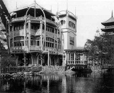 an old black and white photo of a building on the water's edge with a clock tower in the background