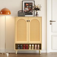 a cabinet with many pairs of shoes on it next to a floor lamp and pictures