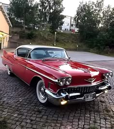 an old red and white car parked in front of a yellow building on a cobblestone street