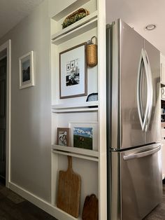 a stainless steel refrigerator in a kitchen with pictures on the wall and shelves above it