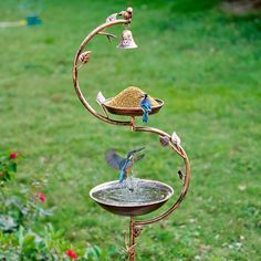 a bird feeder with two birds on it in the middle of a grassy area next to flowers