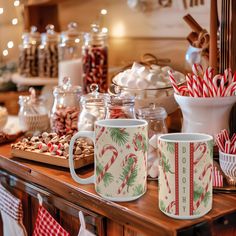 two coffee mugs sitting on top of a wooden table covered in candy canes