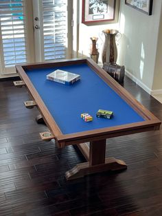 a blue pool table with toy cars on it in a room that has wooden floors and windows