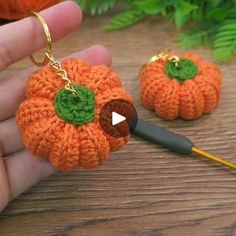 someone is holding two small crocheted pumpkins in their hands, one has a green button on it