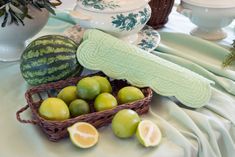 a table topped with green and yellow fruit on top of a white cloth covered table