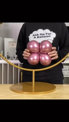 a person holding some pink balls in front of a gold ring on top of a table