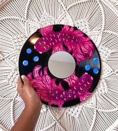 a person is holding up a pink and black disc with blue dots around it on a white doily