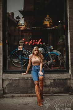 a woman sitting in front of a store window with her leg up on the ledge