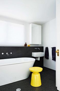 a white bath tub sitting next to a sink and a yellow stool in a bathroom