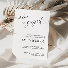 a white wedding card with the words we're engaged on it next to some feathers