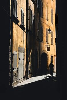 a person walking down an alley way with buildings in the background and sunlight shining on them