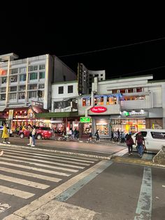 people are crossing the street in front of some buildings at night with cars and pedestrians