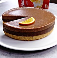 a chocolate cheesecake with an orange slice on the side and a carton of yogurt behind it