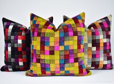 three colorful pillows sitting next to each other on a white surface and one is made out of different colored squares